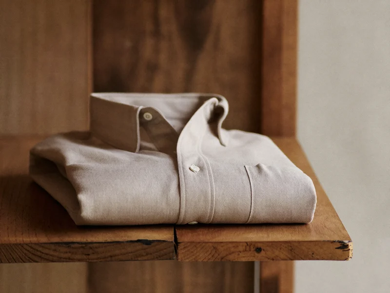 Chemise en lin sable pliée sur une étagère en bois, lumière naturelle
