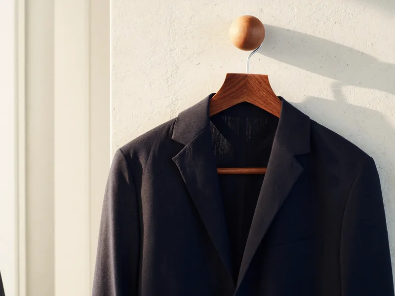 Veste d'été marine non structurée suspendue sur un cintre en bois contre un mur blanc