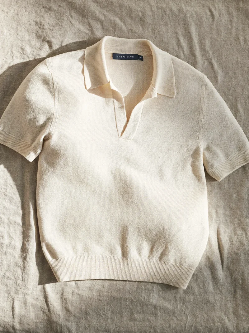 Polo en maille fine écrue posé à plat sur une toile de lin naturelle